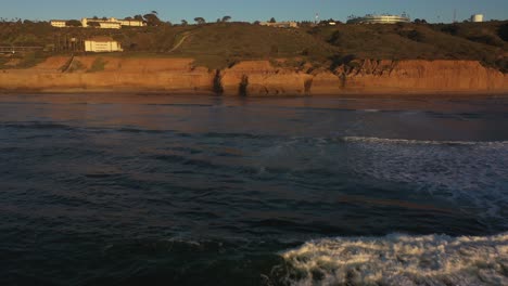 Una-Impresionante-Toma-De-Dron-Captura-La-Hora-Dorada-De-La-Puesta-De-Sol-Mientras-El-Dron-Vuela-Bajo-Sobre-El-Agua-Brillante,-Acercándose-A-Los-Majestuosos-Acantilados-Que-Se-Encuentran-Más-Adelante