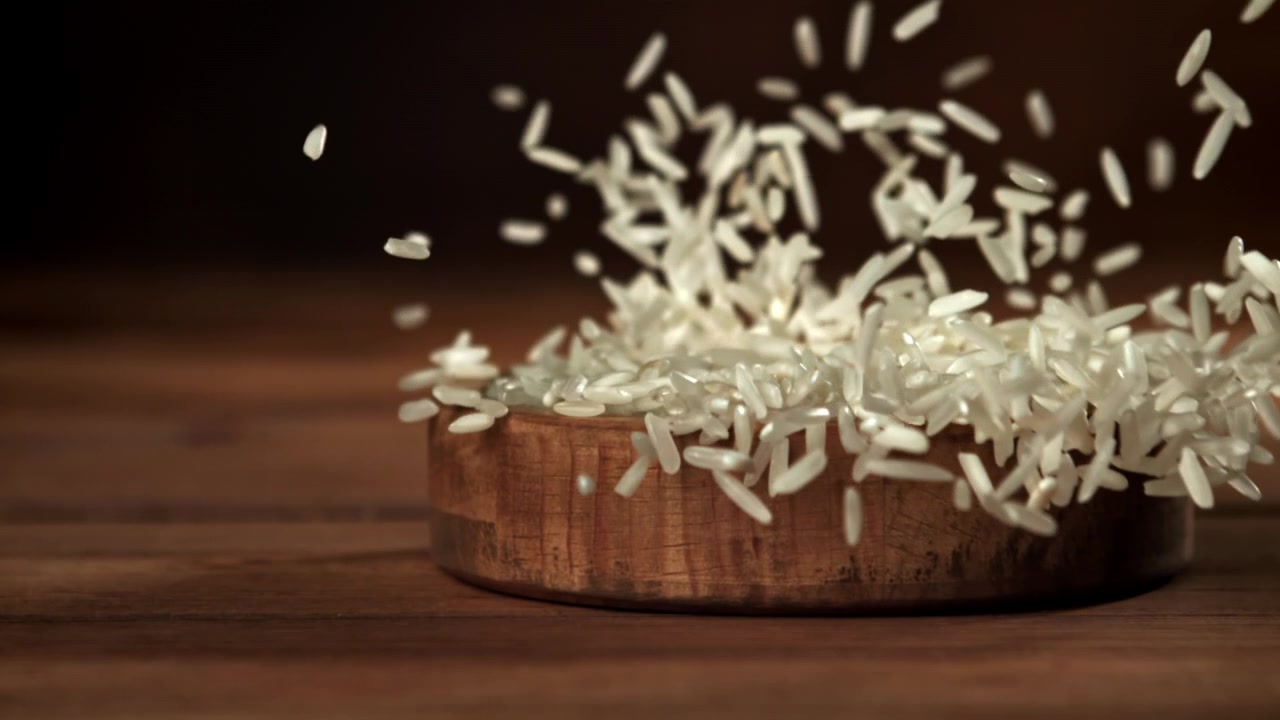 Chicchi di riso bianco che si versano in una ciotola di legno.