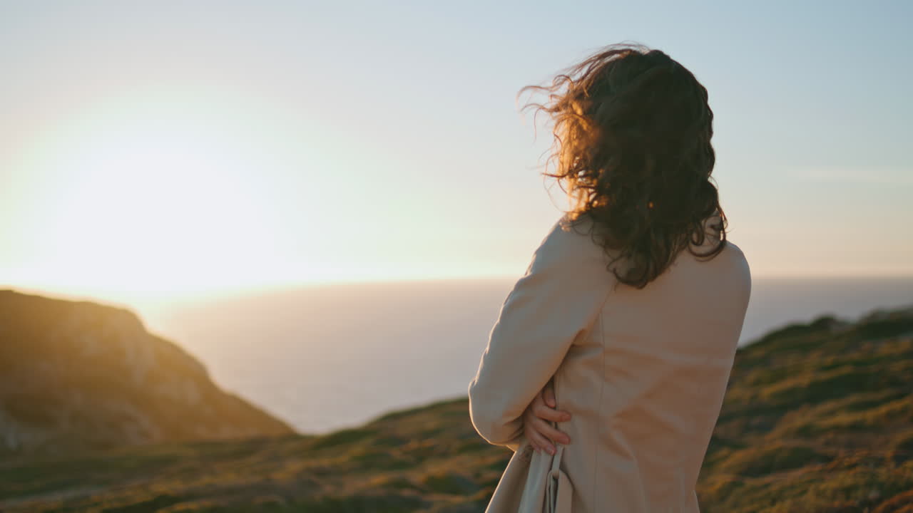 바다의 수직에서 해가 지는 것을 지켜보는 사려 깊은 여자.