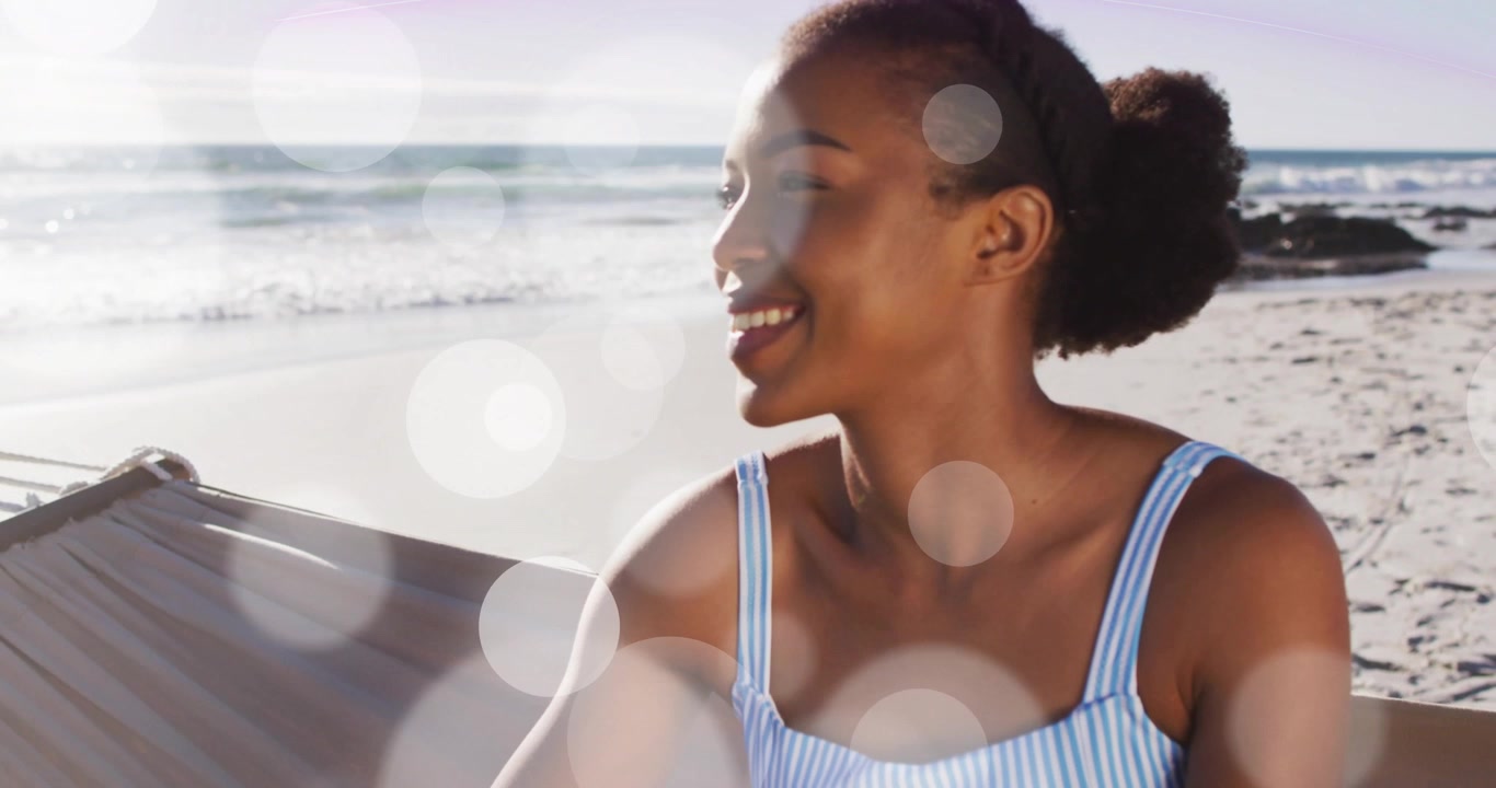 Donna seduta su un'amaca in spiaggia, la luce del sole crea un effetto bokeh sul viso, che si gira e sorride per benessere