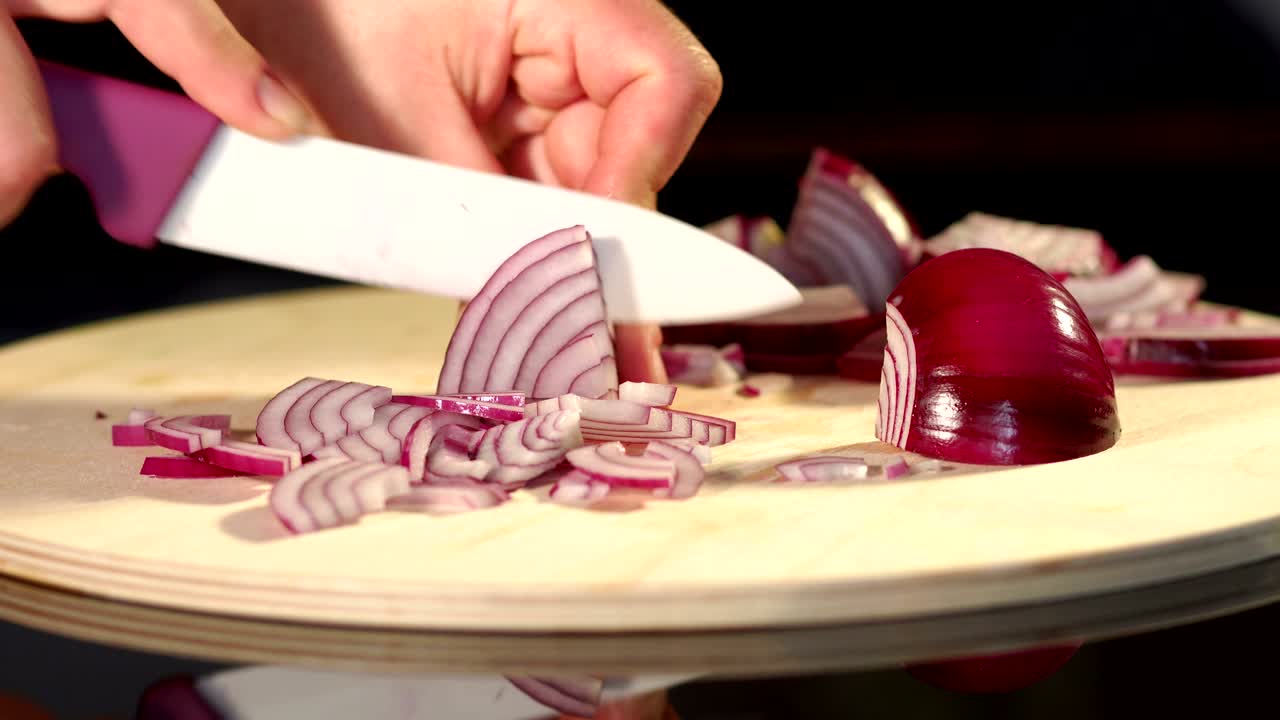 A girl is cutting a red onion on a cutting board.