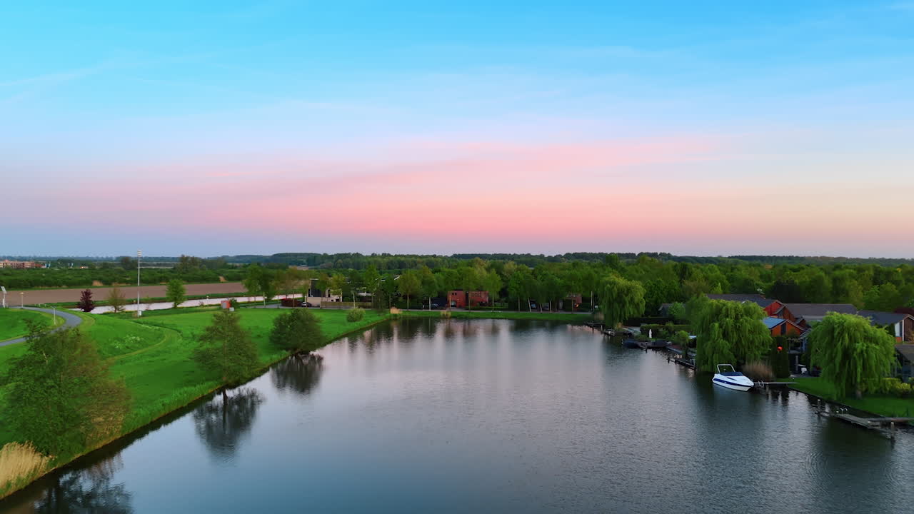 Sunset over a calm river. Calm water reflects vibrant sunset colors above a lush landscape with boats near houses along the riverbank