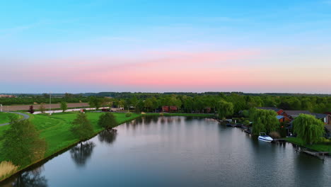sunset over a calm river. calm water reflects vibrant sunset colors above a lush landscape with boats near houses along the riverbank