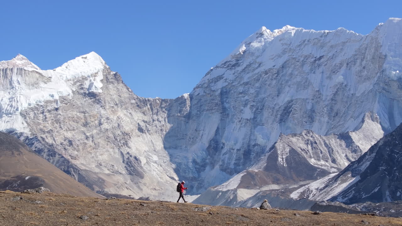 Ripresa drone con effetto parallasse di un viaggiatore solitario che fa trekking al Campo Base del Kangchendzönga a Taplejung, Nepal, con imponenti montagne himalayane innevate che si ergono sullo sfondo.