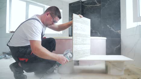obrero cortando baldosas de cerámica con una máquina útil en el sitio de construcción en el interior. reparador corta una baldosa en una esquina