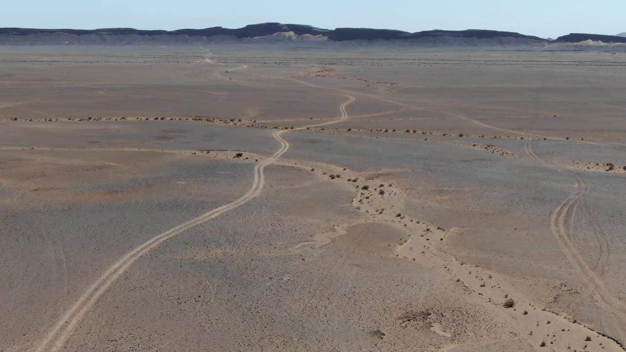 Tire marks on desert landscape in Errachidia region of Morocco near Gara Medouar rock formation. Aerial birds eye pov