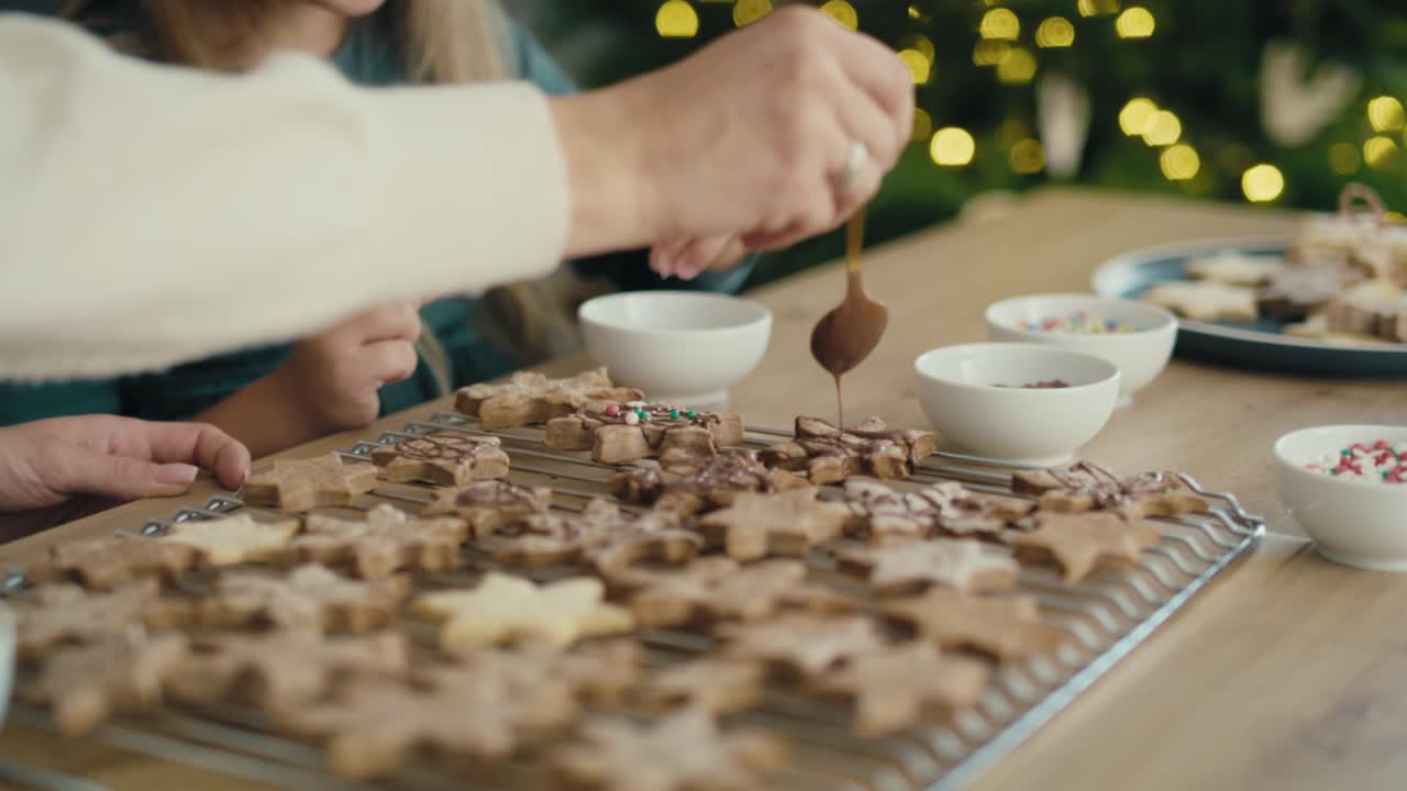 madre y hija caucásicas decorando galletas de pan de jengibre con chocolate y salpicaduras.