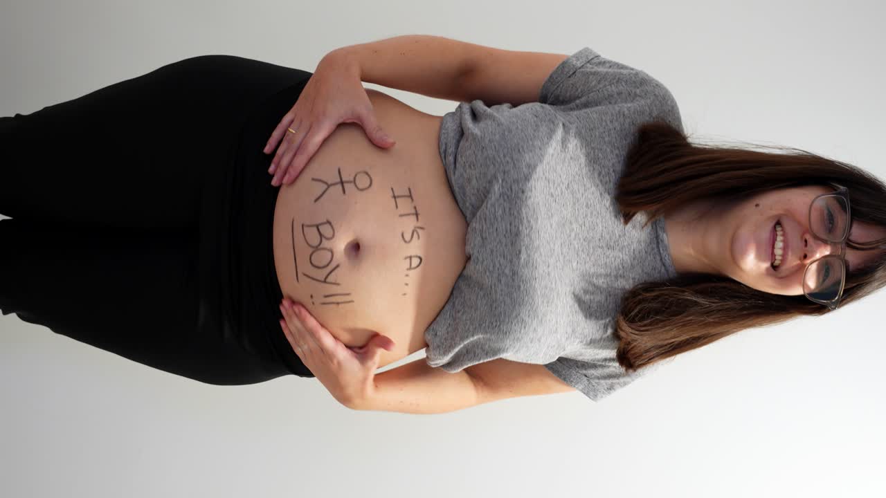 Happy pregnant woman looks at belly with It's a boy written, 4K. Vertical