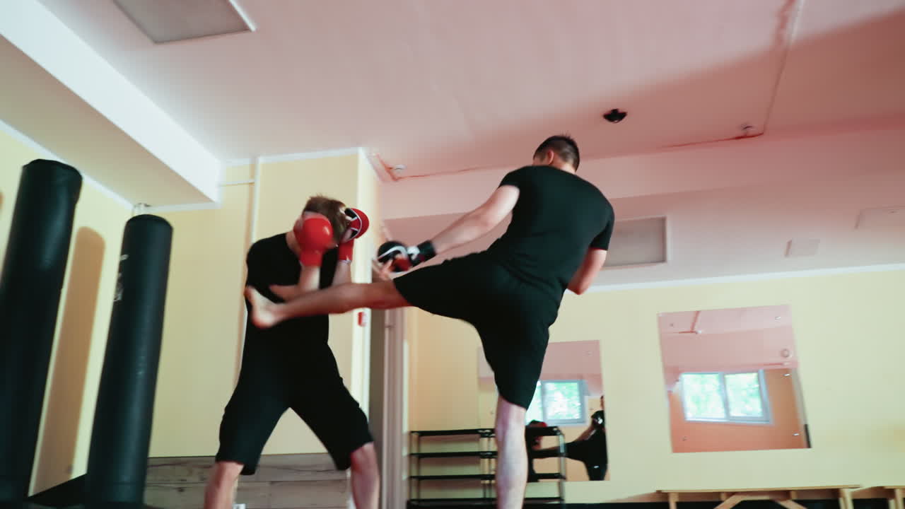 Fighters training in martial arts gym, one executing strong knee strike while opponent defends with gloves, showcasing intensity, strength, endurance, and discipline during sparring session