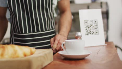 video of midsection of diverse male seller in coffee shop and customer paying by smartphone