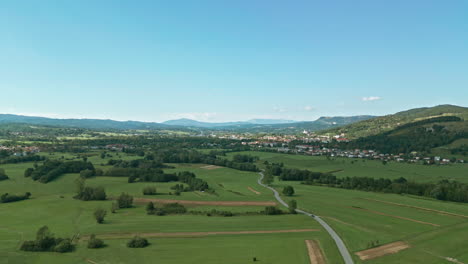 a slow drone fly over a field of meadows, fields and a road over a clear sky with hills in the background