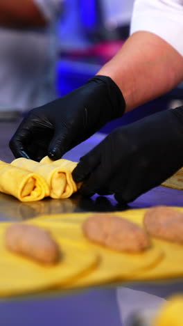 preparing the crepes stuffed with fried minced meat. factory worker rolling the stuffing into a yellow thin pancakes. blurred foreground. vertical video
