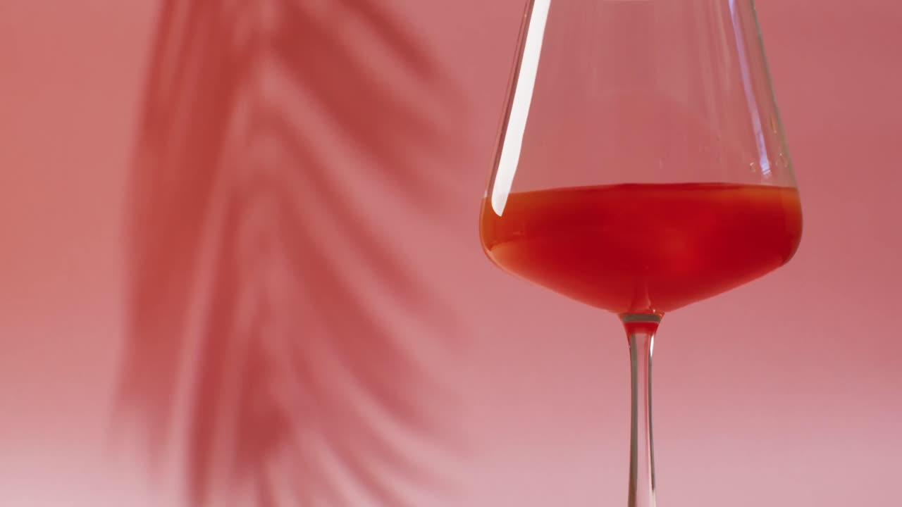 Primo piano di bevanda in bicchiere con ombra di foglia su sfondo rosa