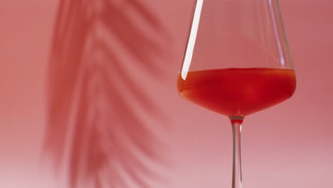 Close-up-of-drink-in-glass-with-shadow-of-leaf-on-pink-background