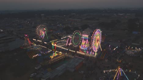 Primer-Plano-Aéreo-De-Drones-De-Un-Parque-De-Atracciones-Indio,-Rueda-De-Ferris-Y-Diferentes-Paseos-En-La-Iluminación-Nocturna-En-La-Feria-Comercial-De-Gwalior,-India