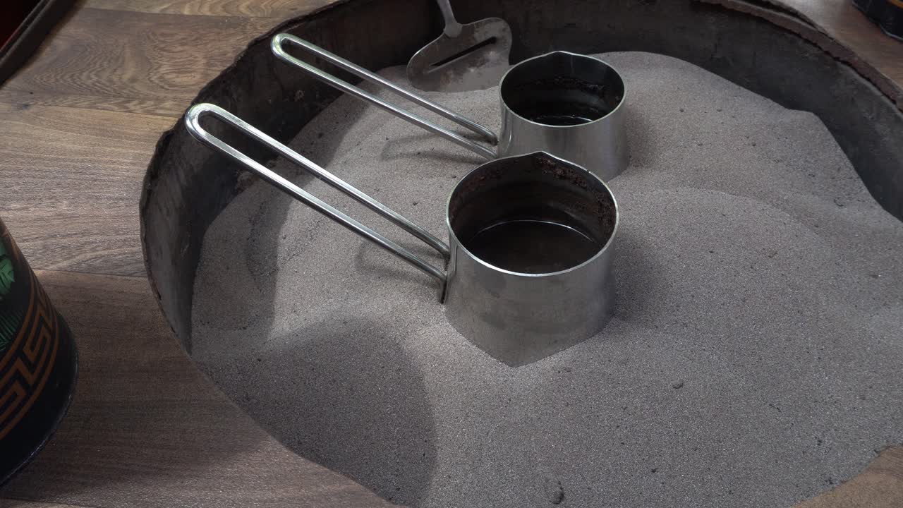 Two pots boiling for Moroccan coffee placed in the sand