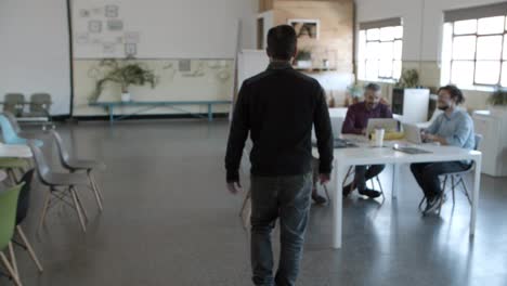 back view of young man walking to cheerful colleagues