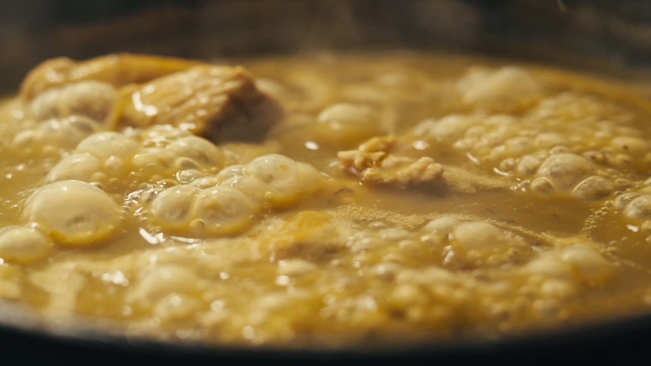 Green boiling sauce with chicken texture close-up macro. Cooking green chicken curry with spices by wooden spoon at home.
