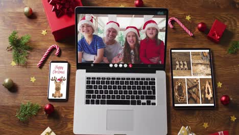 Family-wearing-snatas-hats-on-video-call-on-laptop,-with-smartphone,-tablet-and-decorations