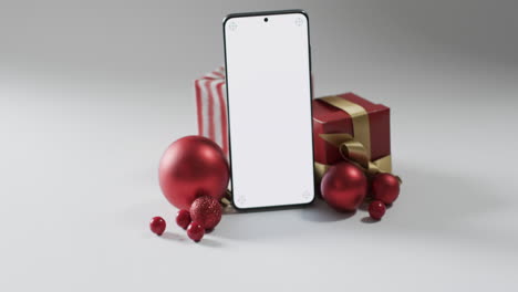 Video-of-christmas-presents,-baubles-and-smartphone-with-copy-space-on-white-background