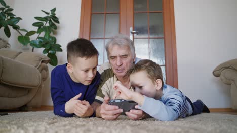 two grandchildren are teaching grandfather to play their favorite toy on the tablet in the free time of the day. modern technologies