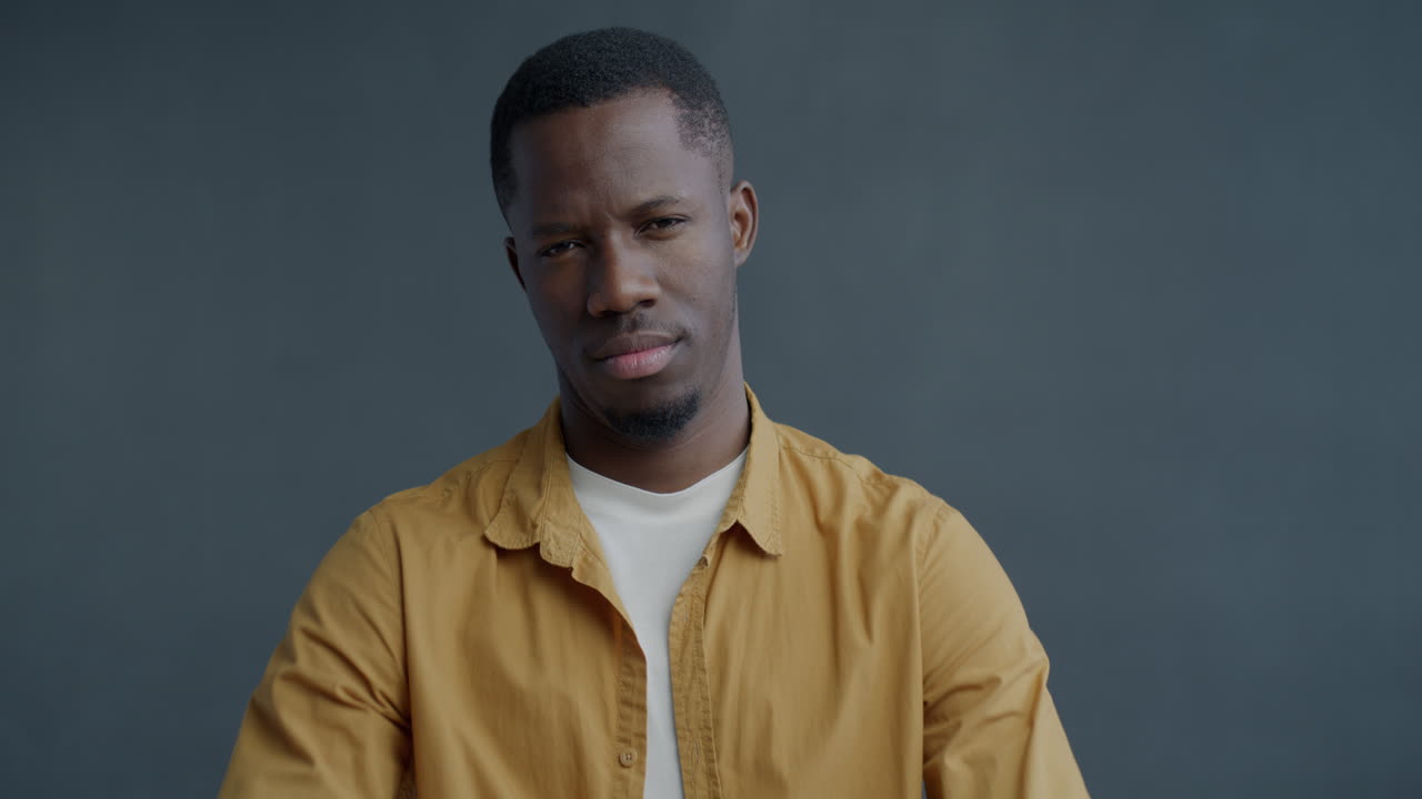 Man with neutral expression in a yellow shirt
