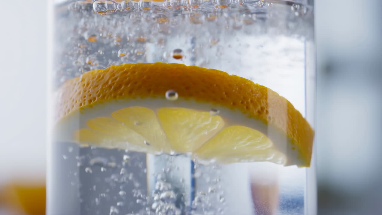 Lemon Slice In Sparkling Water, Closeup Macro Showing Orange Rind Resting On Glass Rim, Effervescent Bubbles