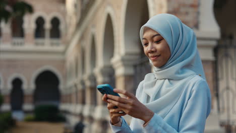young muslim woman using smartphone near a historic building