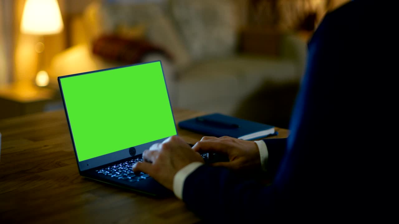 en casa, el hombre se sienta en su escritorio y escribe en una computadora portátil con pantalla verde. su apartamento está hecho en colores amarillos y es cálido.