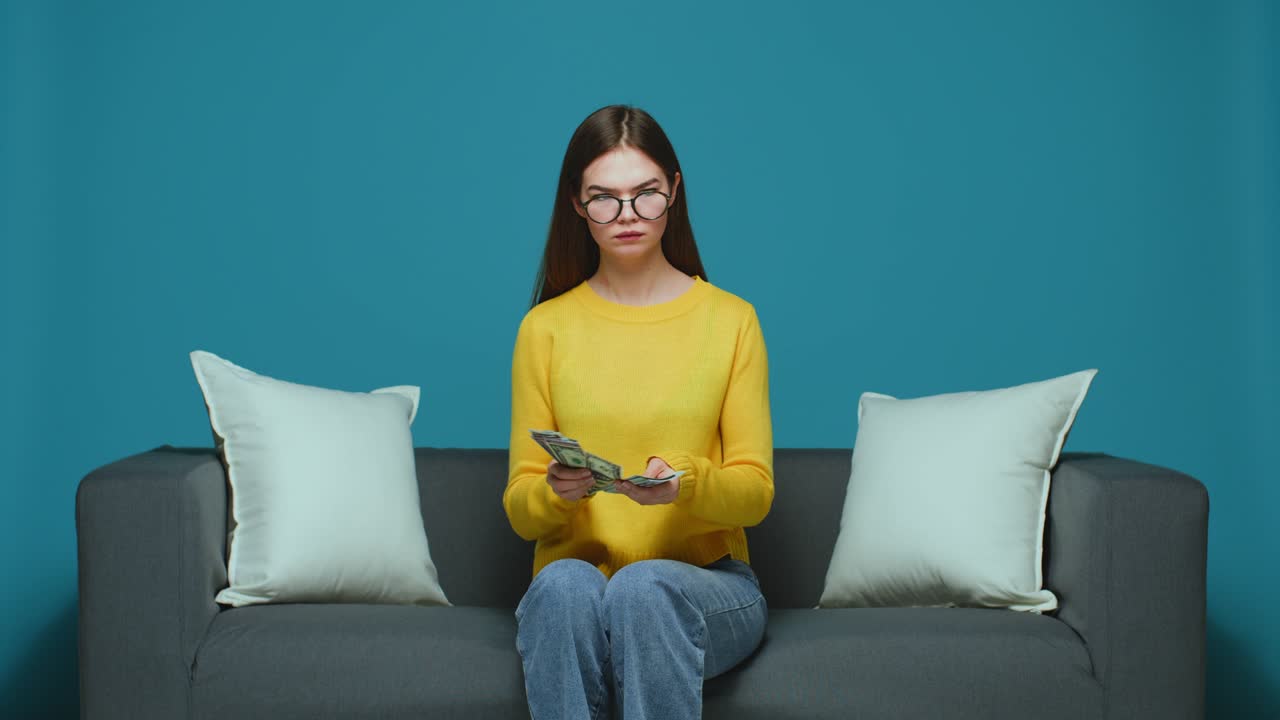 심각한 젊은 소녀는 현금을 계산하고 재정 문제, 은행, 소파에 앉아 재정 부족에 대해 걱정합니다.