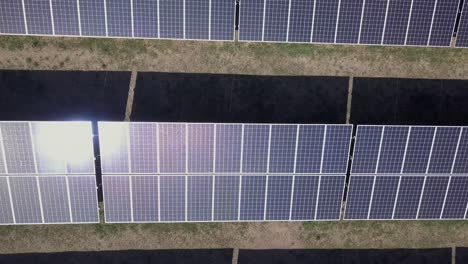 Sun-energy-reflects-in-black-solar-panels,-low-aerial-dolly-shot