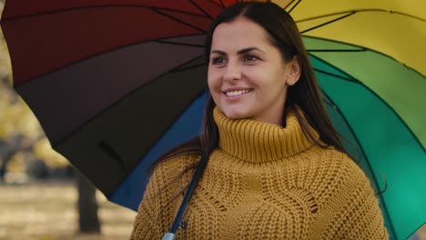 caucasian woman walking with colourful umbrella at park.