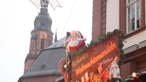 Adornos-De-Papá-Noel-En-El-Techo-De-La-Plaza-Principal-De-Heidelberg,-Cerca-De-La-Catedral,-En-Un-Mercado-Navideño-Festivo-En-Europa