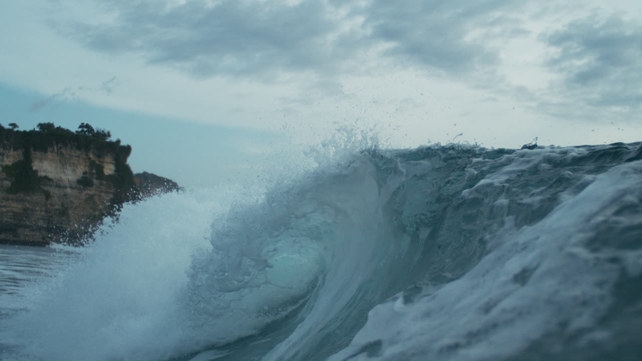 Tight foamy frothing breaking ocean wave forming a barrel near the shore, slow motion texture