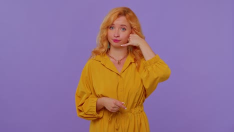 Cheerful-girl-in-yellow-dress-looking-at-camera-doing-phone-gesture-like-says-hey-you-call-me-back