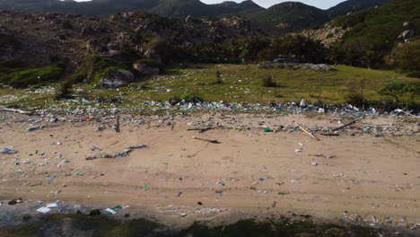 aerial trucking of trash,waste and dirt on sandy beach in vietnam during sunlight - environmental pollution of earth in asia - beautiful mountain landscape in background