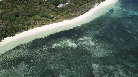 Drone-aerial-rise-and-pan-down-to-tropical-island-with-boats-on-the-tropical-blue-water