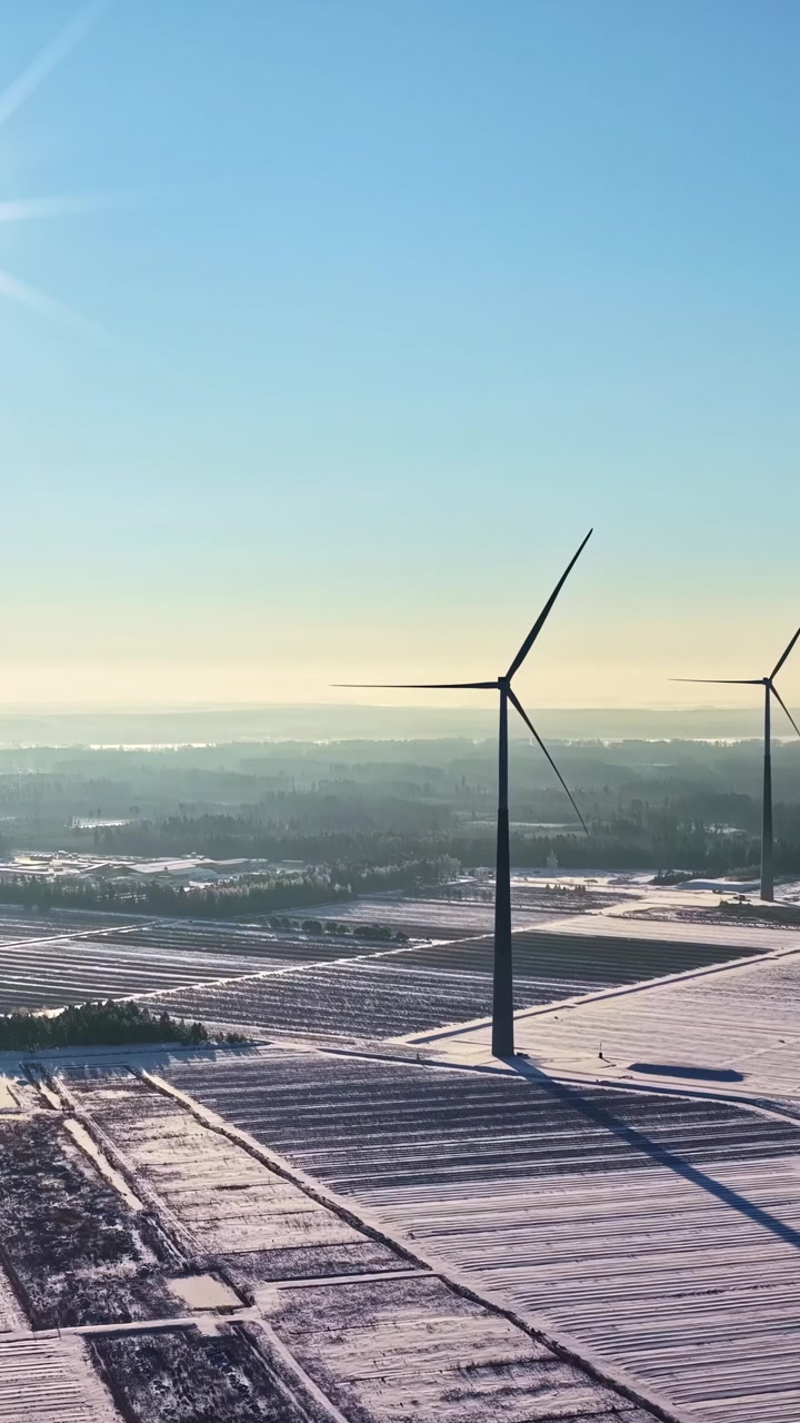 Luftfoto af en vindmøllepark på en solrig vinterdag, med turbiner der genererer ren energi.