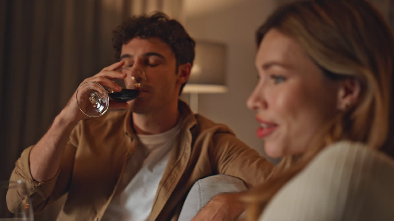Relaxed spouses drinking wine relaxing together at cozy home evening close up.