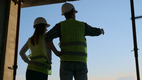 Dos-Ingenieros-Jefe-Con-Un-Dibujo-En-La-Mano-Mirando-El-Sitio-De-Construcción.-Vista-Desde-Atrás.-Ingeniero-Jefe-Con-Plano-En-Mano-Mirando-La-Construcción