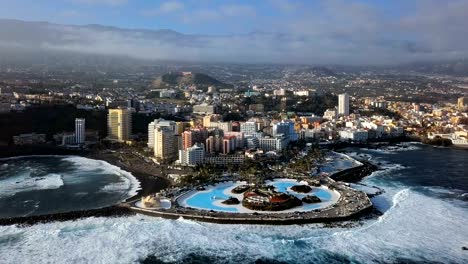 aerial panorama of puerto de la cruz resorts and pools surrounded by sea waves, tenerife, canary islands, spain.