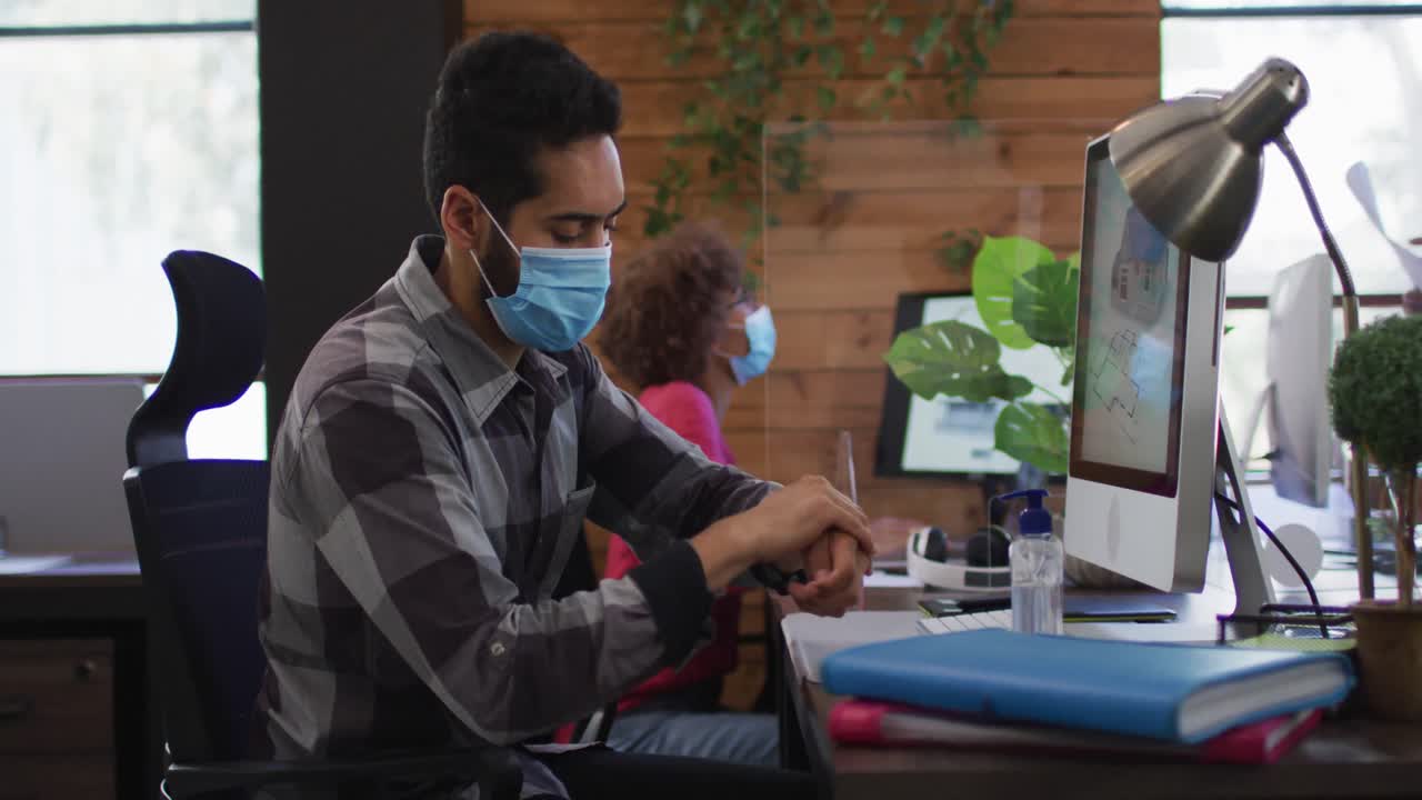 Middle eastern man wearing face mask using hand sanitizer at modern office