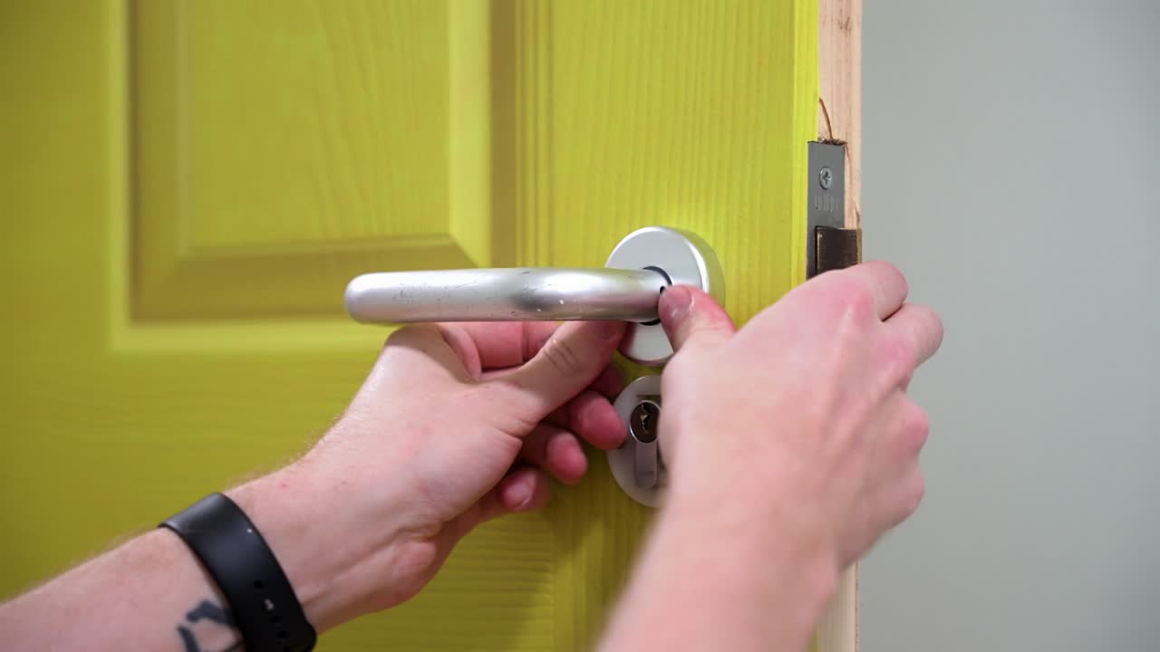 Tradesman wearing a watch fitting and installing a silver door handle to a green door close up
