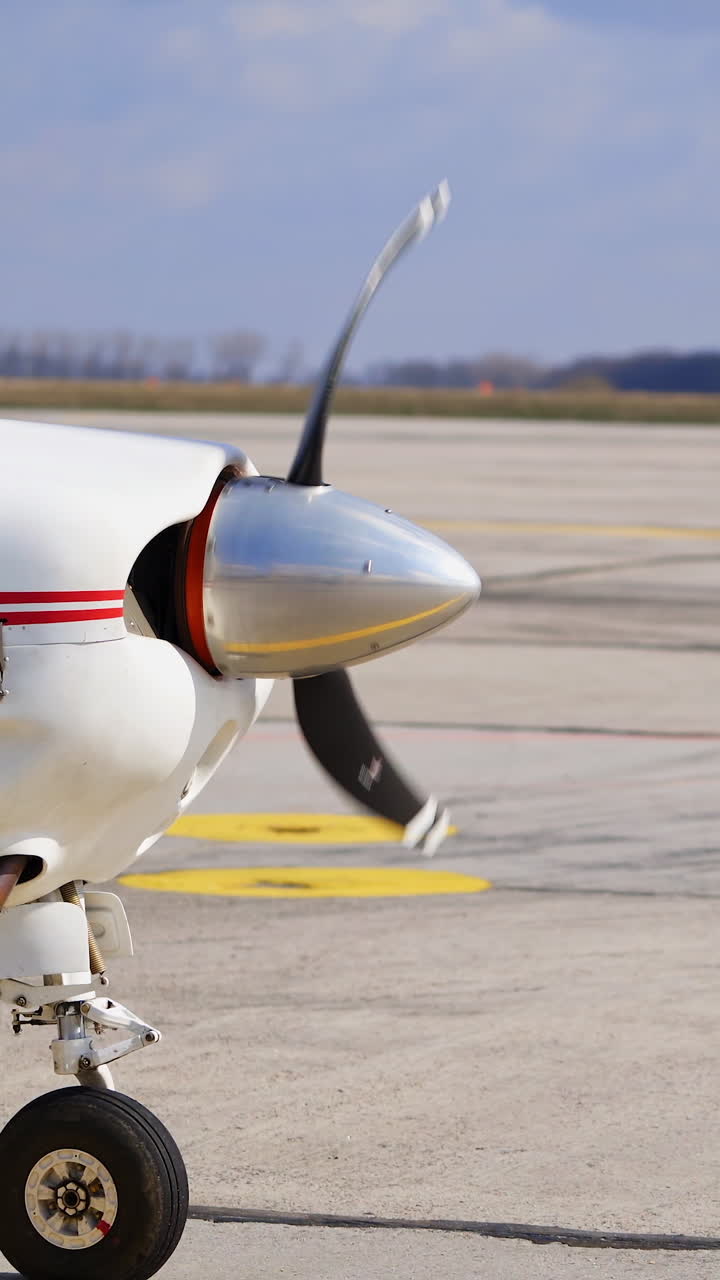 The propeller of a small white aircraft with red lines rotating. Starting the plane before the departure. Vertical video