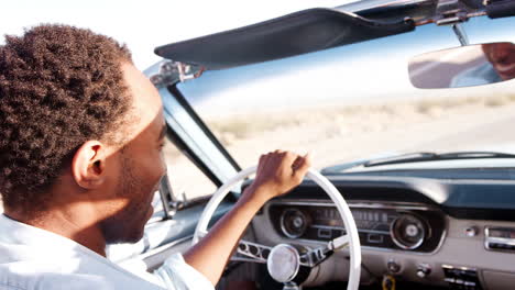 black man driving open top car on desert highway, close up