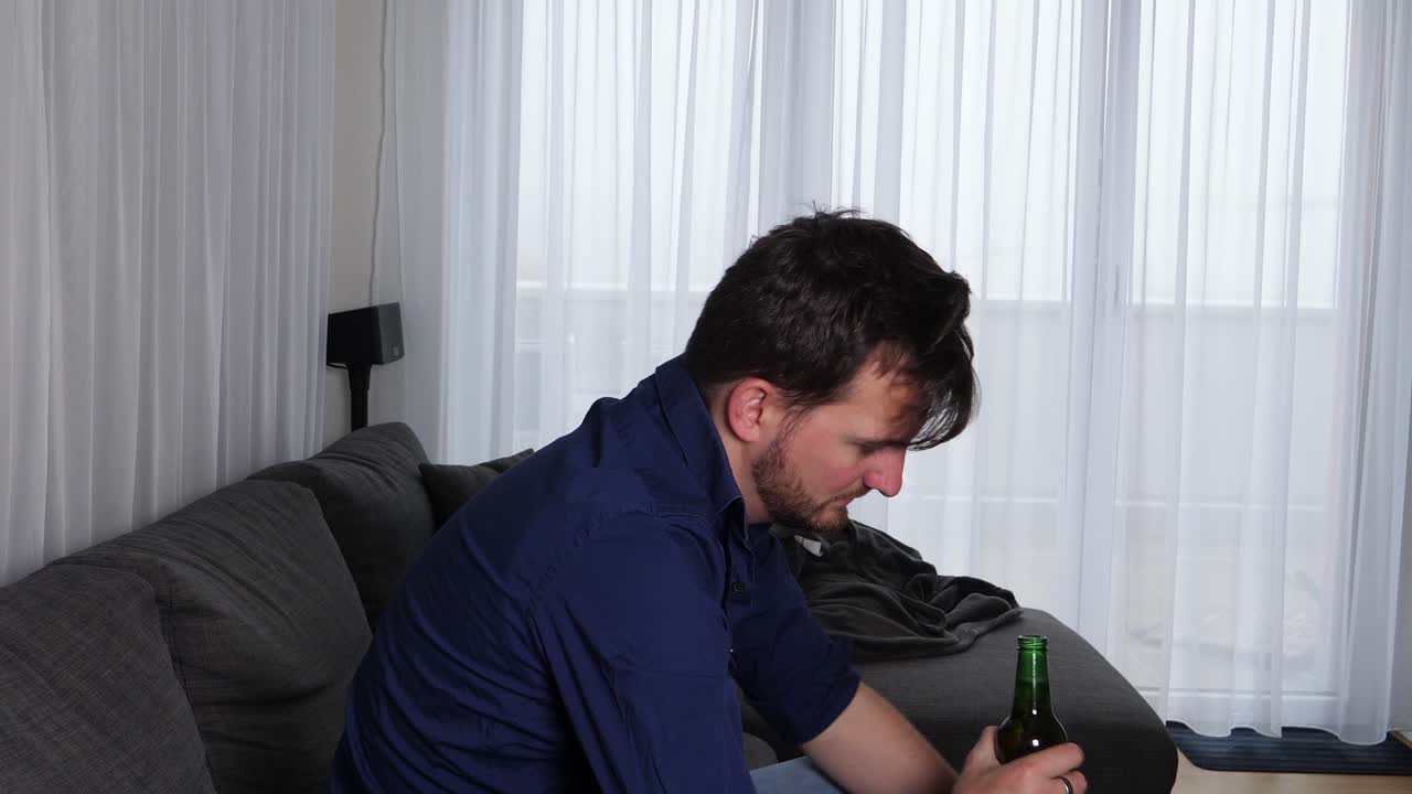 joven alcohólico abriendo una botella de cerveza y recostándose en su sofá