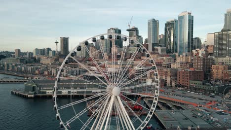 drone flyover above seattle ferris wheel to reveal dense urban buildings and skyline at sunset