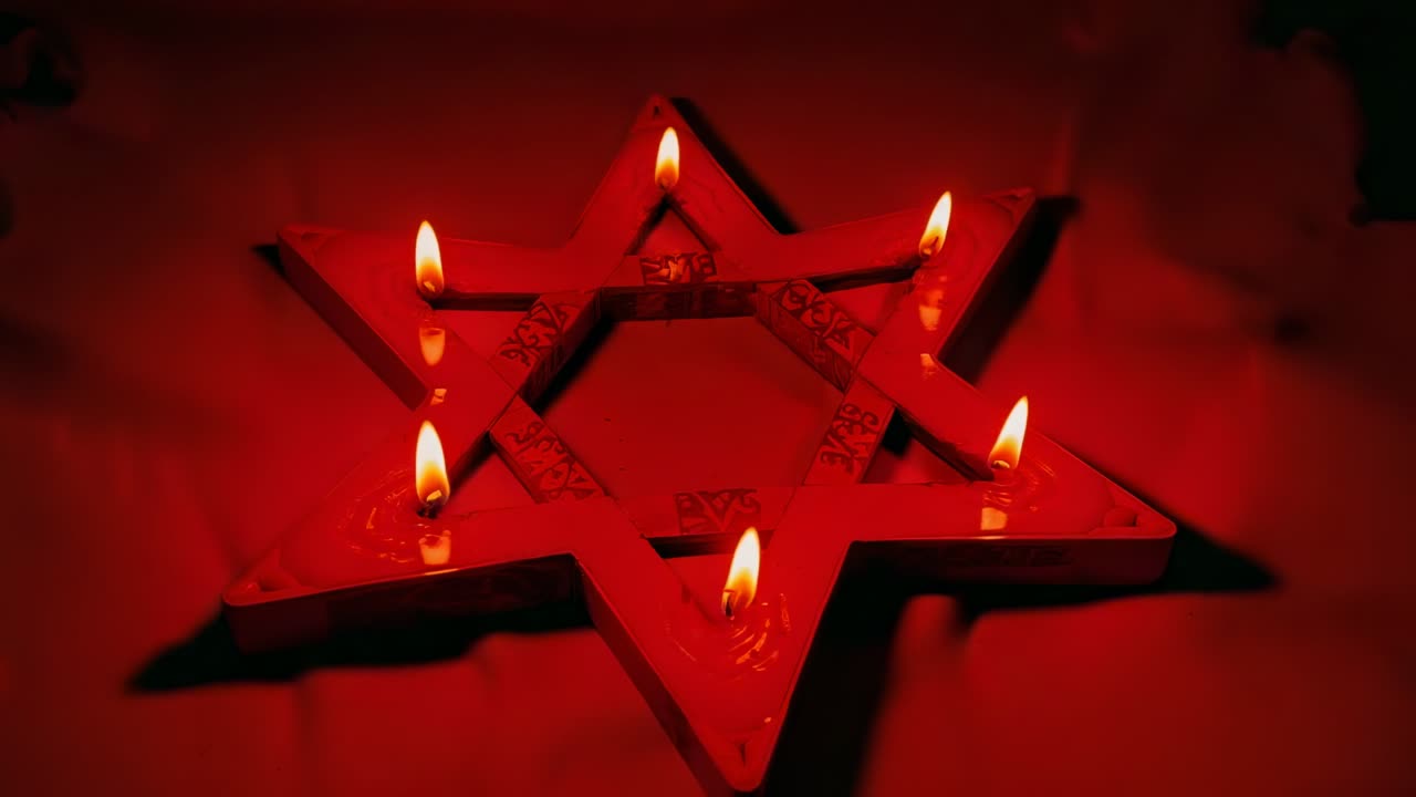 Pulling back camera revealing star lamp holder on cloth table in dimly-lit room, holding six flames