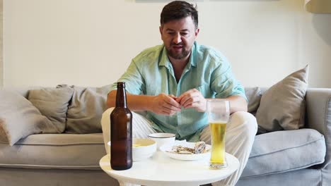 a man relaxing on a couch, eating snacks and drinking beer