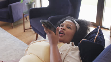 Mujer-Afroamericana-De-Talla-Grande-Tumbada-En-El-Sofá-Y-Hablando-Por-Teléfono-Inteligente,-Inalterada,-En-Cámara-Lenta